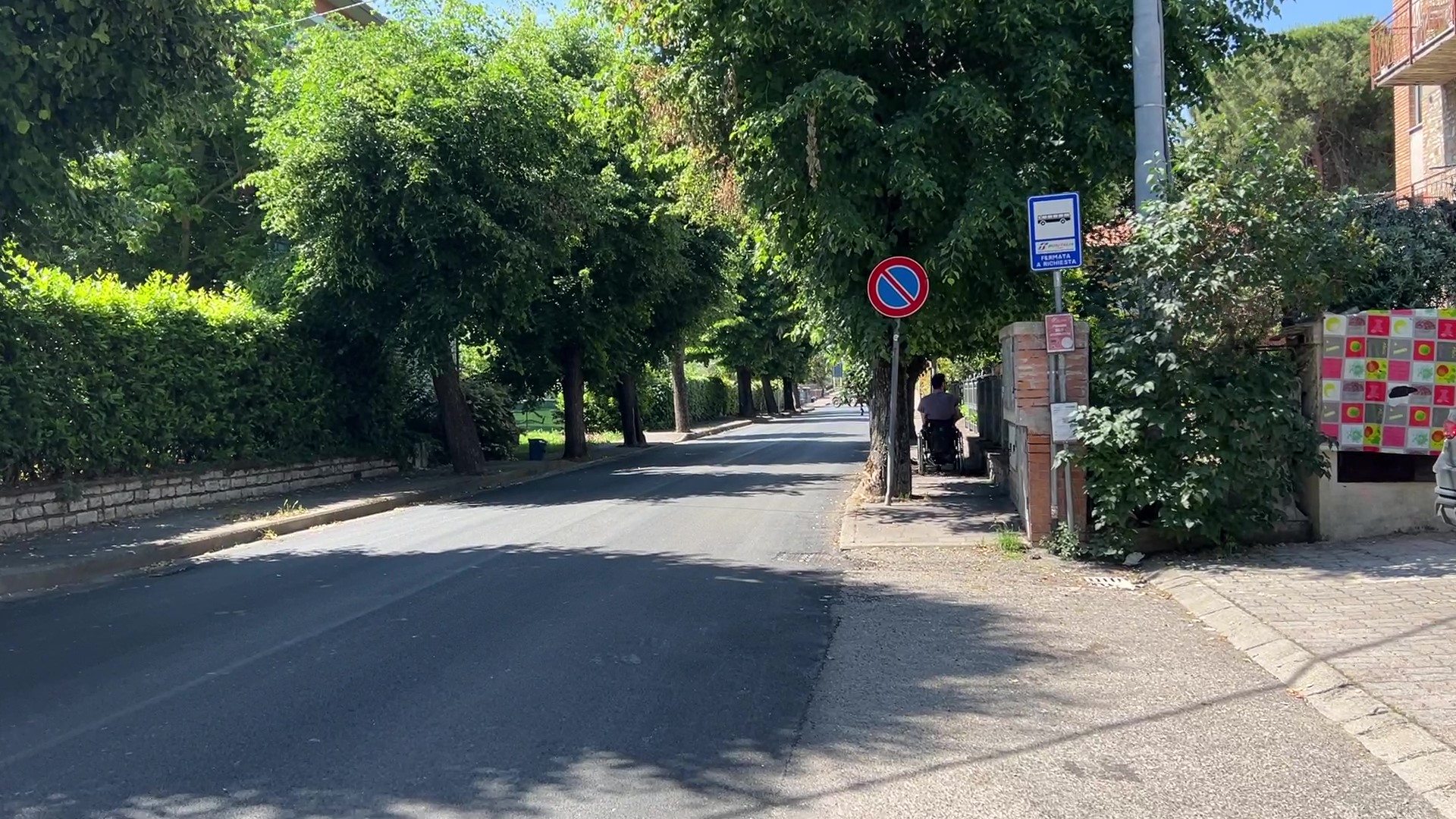 Via del Lavoro in Torricella: von Bäumen gesäumte Straße mit begehbarem Gehweg. Bushaltestelle und keine Parkplätze vorhanden.